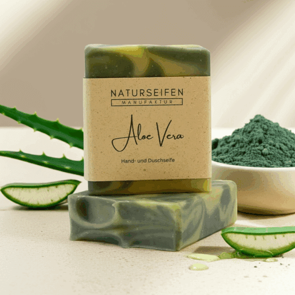 Zwei Stücke handgefertigte Aloe Vera Seife von Naturseifen Manufaktur, eine übereinander gestapelt. Die Seife ist grün marmoriert und hat eine naturfarbene Banderole mit der Aufschrift "Naturseifen Manufaktur Aloe Vera Hand- und Duschseife".