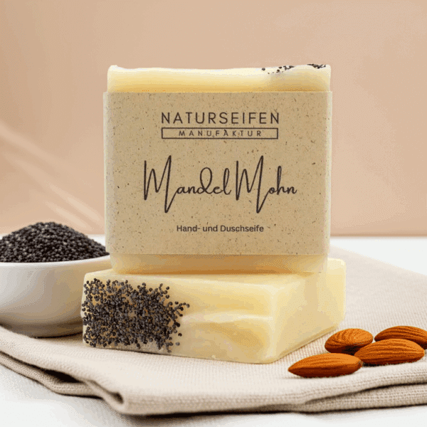 Zwei Stücke handgefertigte Mandel Mohn Seife von Naturseifen Manufaktur, eine übereinander gestapelt. Die Seife ist gelblich-beige mit Mohnsamen und hat eine naturfarbene Banderole mit der Aufschrift "Naturseifen Manufaktur Mandel Mohn Hand- und Duschseife".